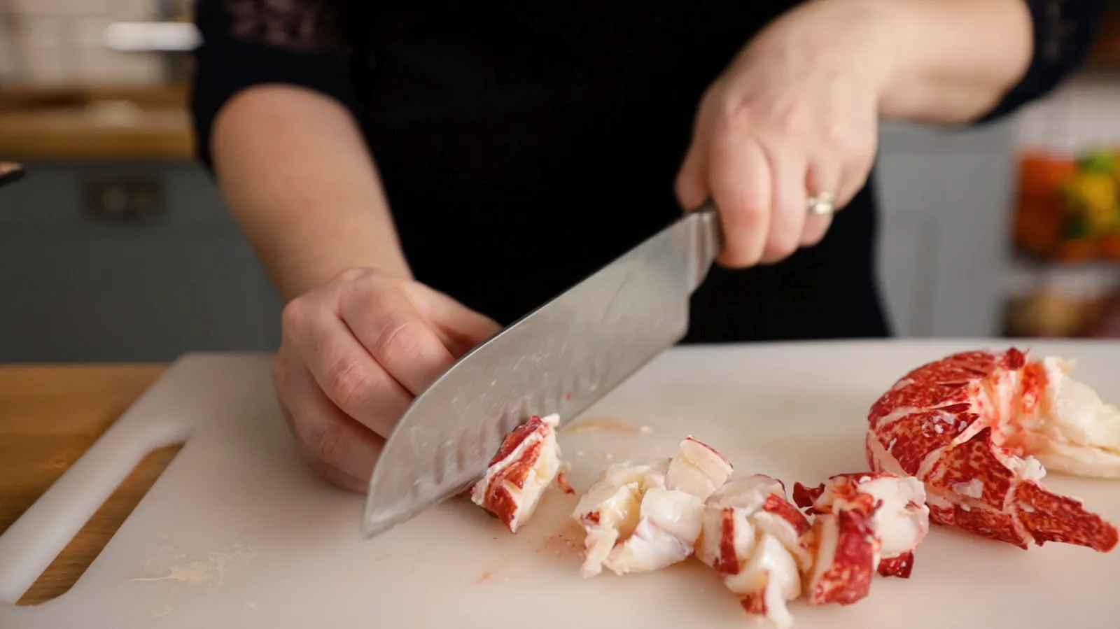 Hands chopping raw meat on a cutting board in a kitchen.