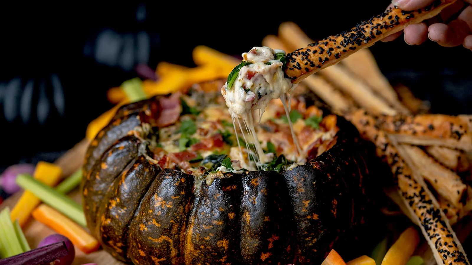 Person dipping food into cheesy stuffed pumpkin