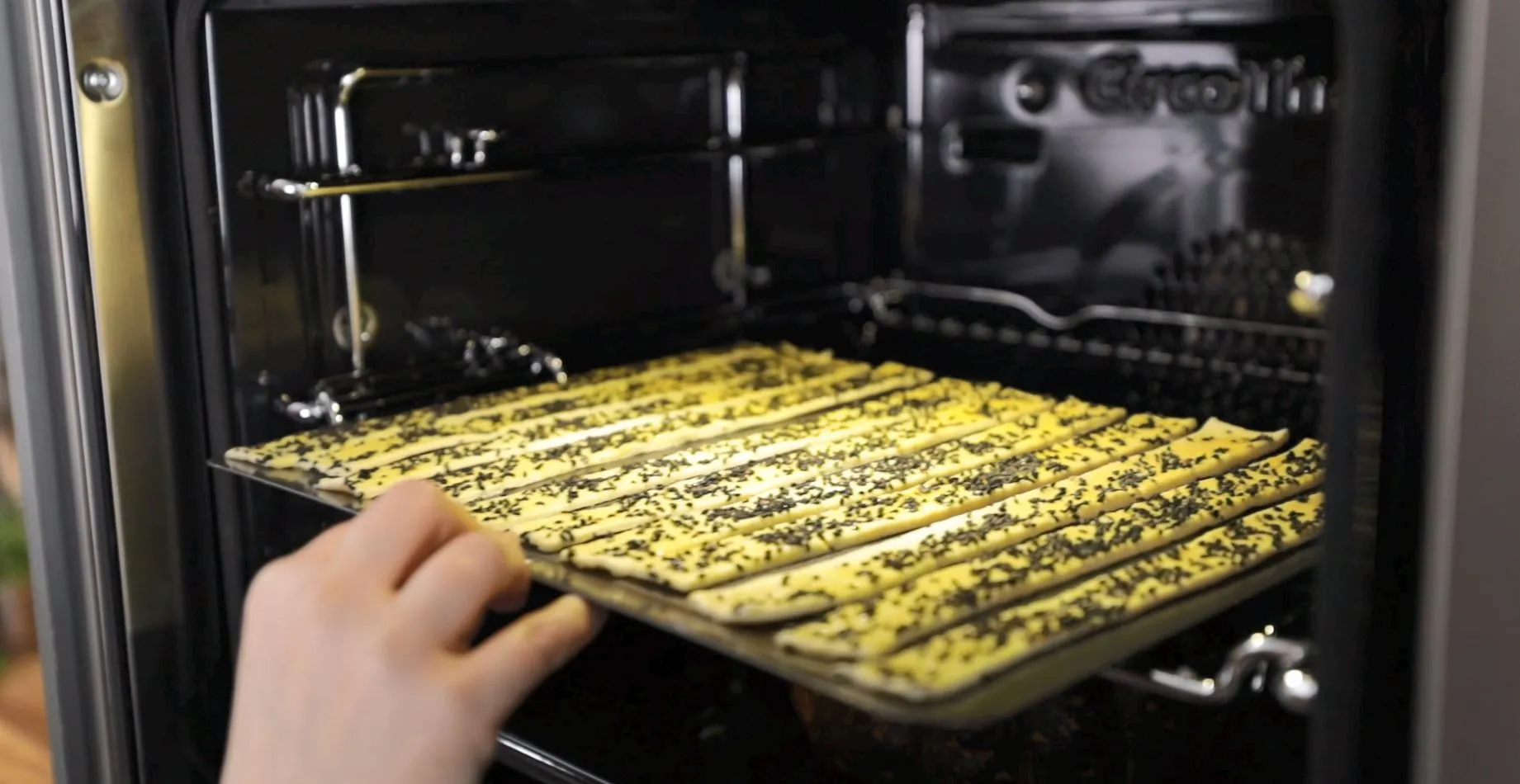 person taking tray of breadsticks out of oven