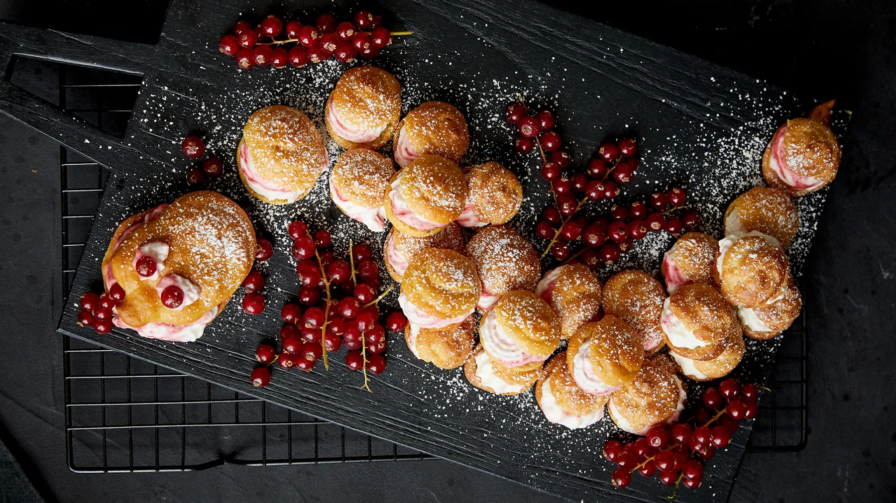Freshly baked pastries, cranberries, and powdered sugar on a dark background.
