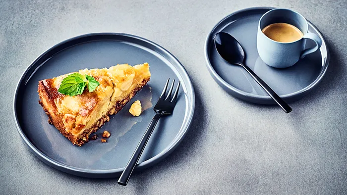 Slice of apple pie, espresso cup, and cutlery on dark plates against a gray background.