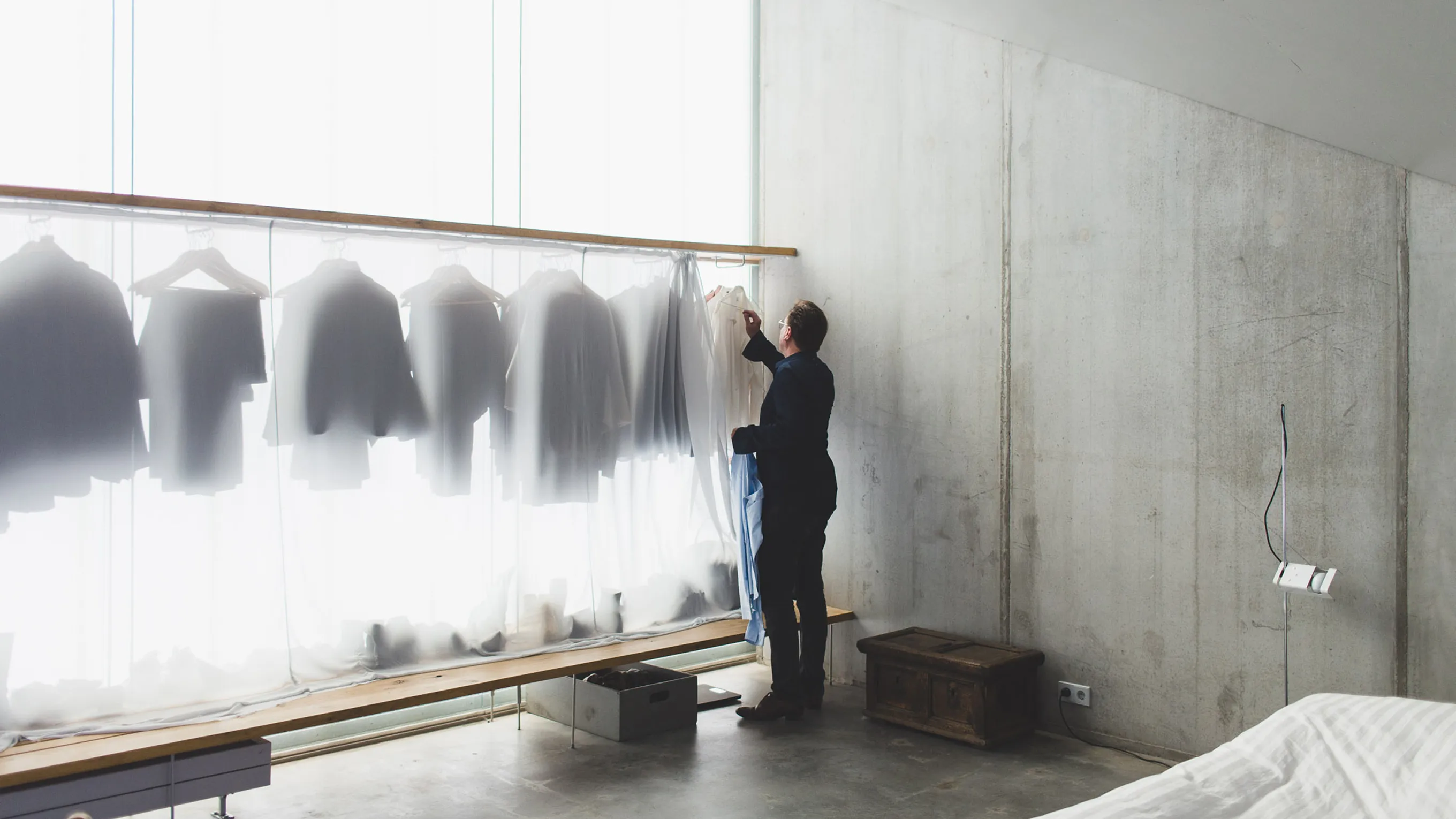 Person hanging clothes on rack in room with white walls and large windows.