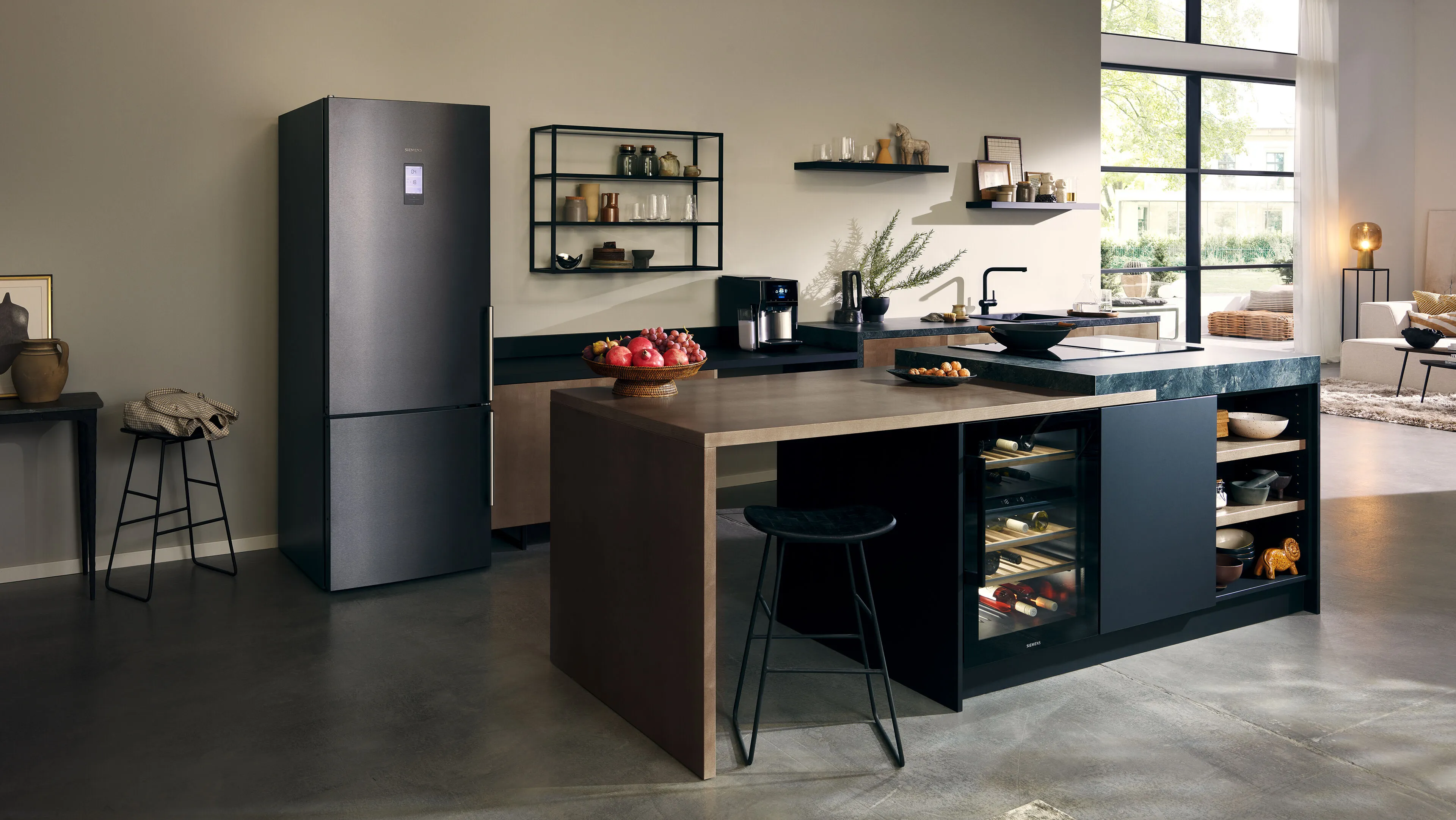 Contemporary open-plan kitchen with a dark fridge, large two-tone island with integrated wine cooler and seating, and floor-to-ceiling windows.