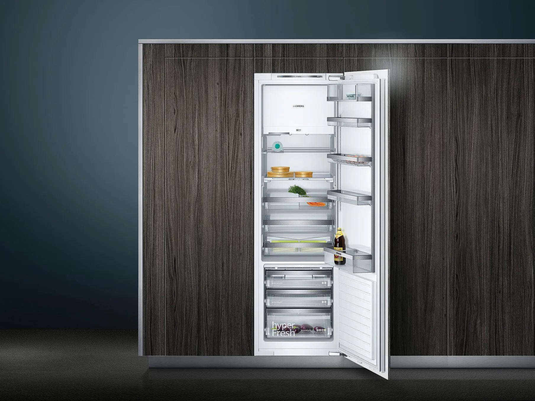 Built-in upright refrigerator with the door open, showing lit glass shelves, door bins, and crisper drawers holding assorted food items.