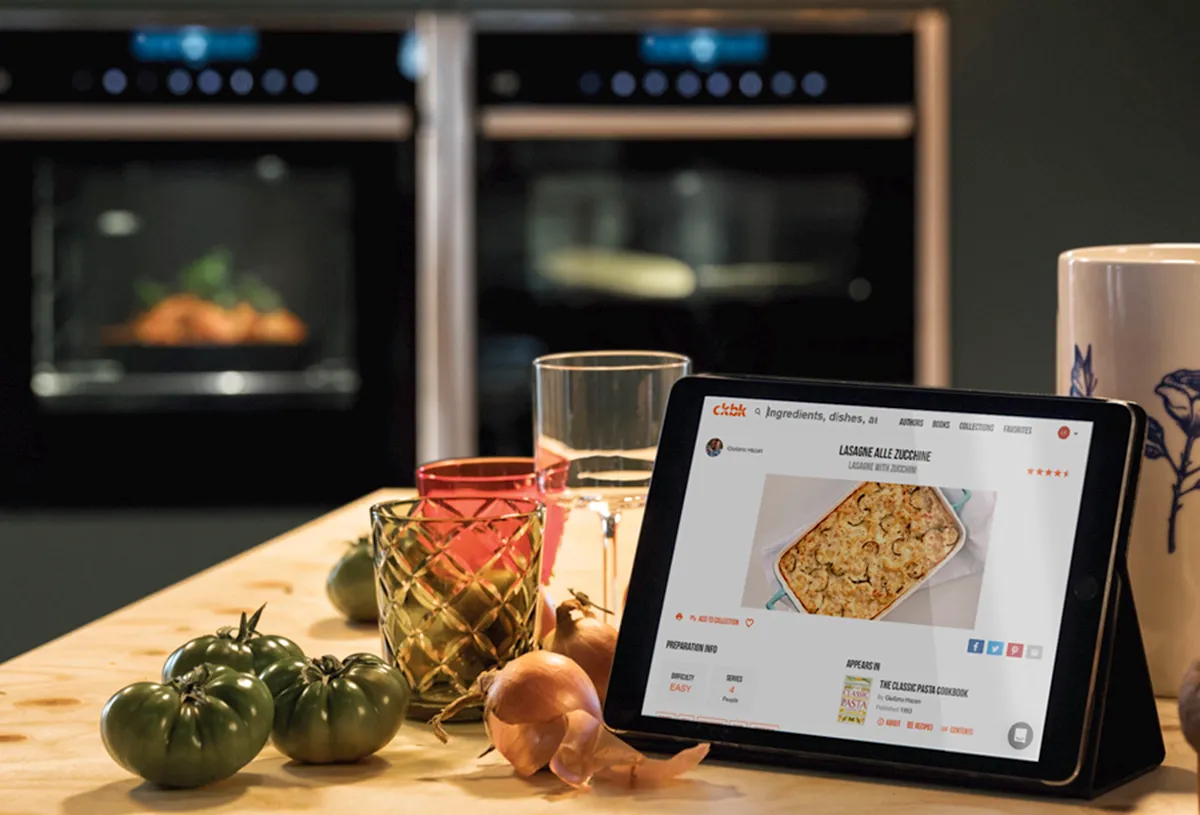 Electronic tablet showing ckbk website on kitchen countertop surrounded by colourful glasses and food