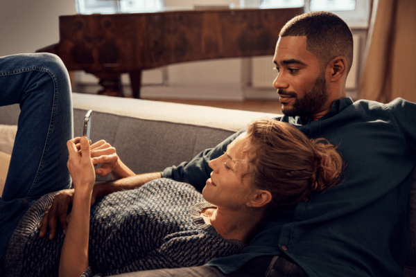 Frau und Mann auf Sofa blicken auf Smartphone