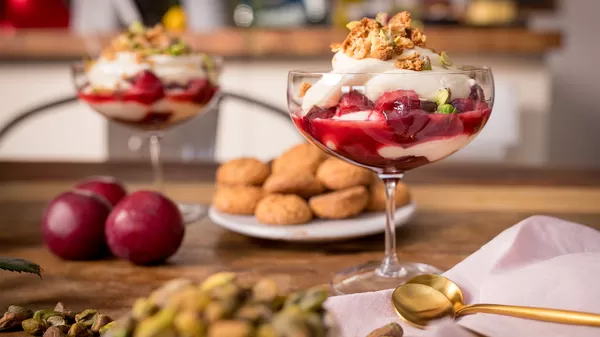 Dessert Parfaits mit roten Früchten, Schlagsahne und knusprigen Tritt, umgeben von frischen Pflaumen und Nüssen.
