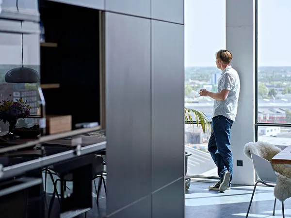 Man standing by window in modern kitchen with city view.