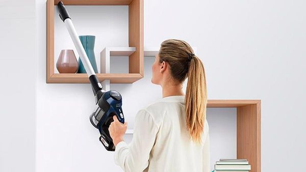 Eine Frau reinigt ein Regal mit einem Bosch Akku-Staubsauger.
