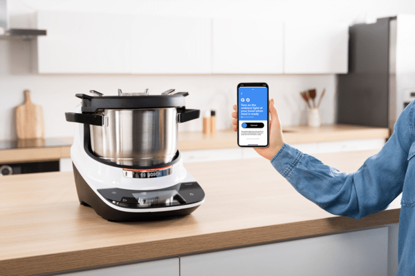 Bosch Cookit steht auf einer Arbeitsplatte. Daneben wird ein Smartphone gehalten mit dem IFTTT Cookit Applet.