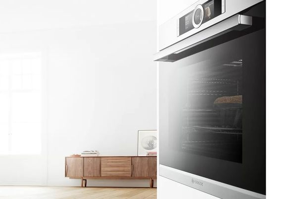 Werkende Bosch-oven met Home Connect op de voorgrond in een woonkamer met een dressoir op de achtergrond