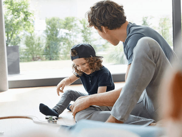 Vader en zoon spelen thuis op de vloer met een speelgoedtrein.