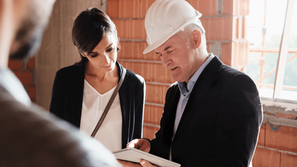 Woman standing next to a construction person looking at a piece of paper in his hands.