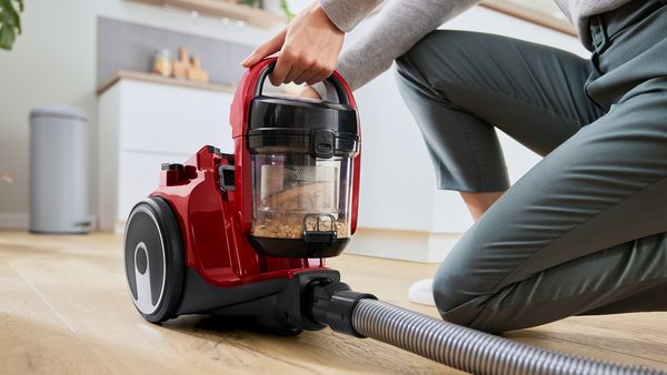 Eine Frau kniet vor ihrem beutellosen Staubsauger von Bosch, um den vollen Beh&auml;lter zu entnehmen.