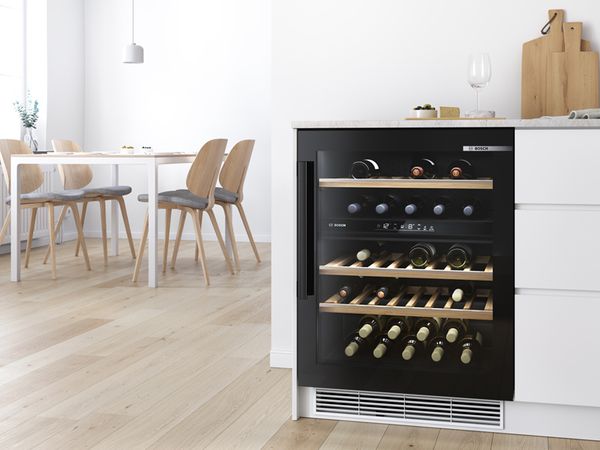 Der Weink&uuml;hlschrank mit Glast&uuml;r von Bosch l&auml;sst den Blick frei auf die Weinsammlung. Moderner, lichtdurchfluteter Essbereich links.