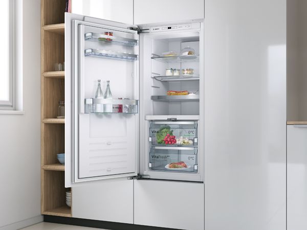 Einbau-K&uuml;hlschrank von Bosch mit offener T&uuml;r, man sieht frische Lebensmittel und Getr&auml;nke im Innenraum.