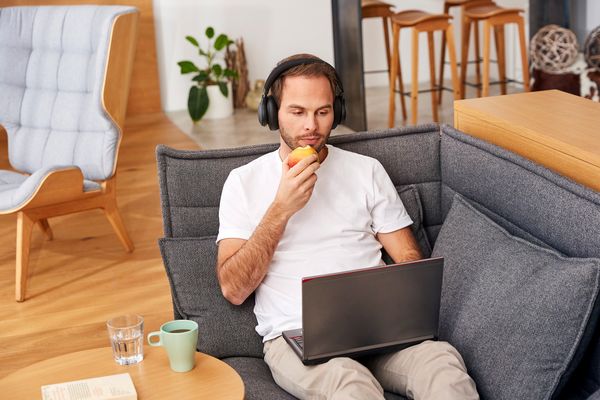 Man eating apple seating on a couch with laptop in his lap