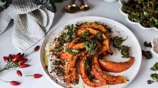 Geröstete orange Squash Scheiben mit knusprigem Kale, Gewürze und garniert auf einem weißen Teller.