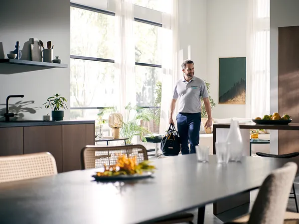 Hombre de pie en cocina moderna con mesa de comedor, estantes y plantas.
