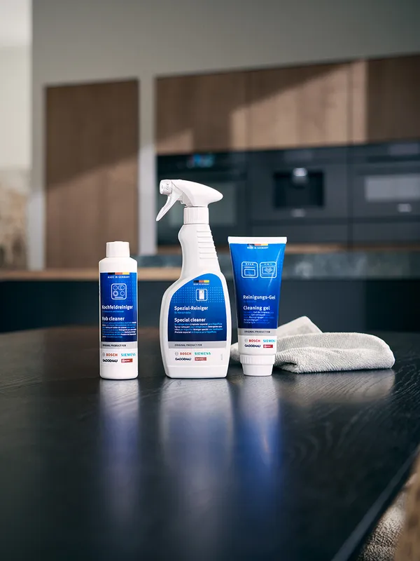 Cleaning products including a spray bottle, liquid cleaner, and cleaning gel, with a microfiber cloth on a dark kitchen countertop.