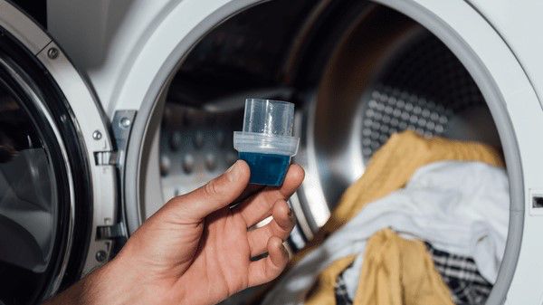 Hand holding detergent in front of open washing machine