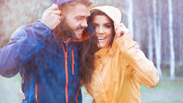 A man in the rain wearing a blue raincoat hugging a woman in orange raincoat