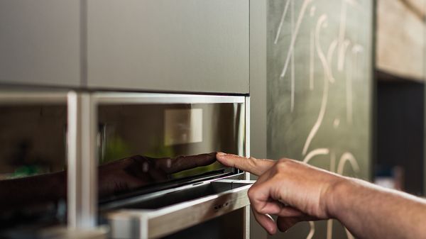 A man’s hand inputting data into oven’s control interface.