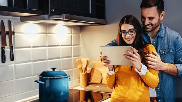 A good looking couple looking at a tablet in a stylish kitchen next to a hob.