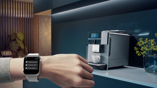 A hand with a smartwatch on a wrist. A smart coffee maker in the background.