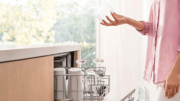Person picking clean glass out of fully loaded dishwasher