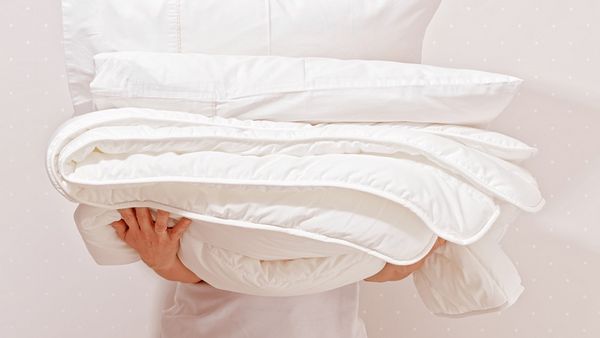 A person holding a stack of comforters and pillows