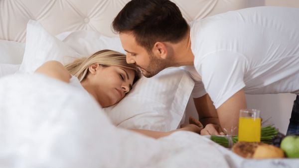 Woman sleeping in a bed with man leaning over her