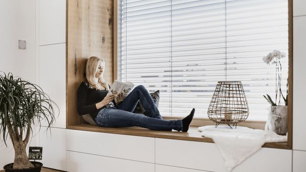 A woman sitting on a window sill in a stylish apartament reading a magazine.