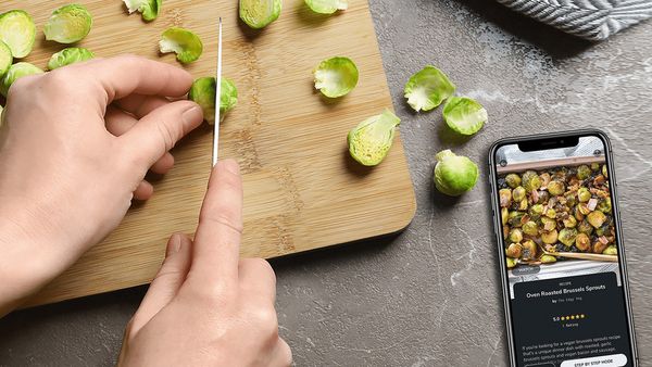 A pair of hands slicing brussel sprouts next to a smarphone featuring SideChef on screen.