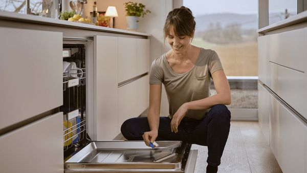 A woman crouching by a dishwasher.