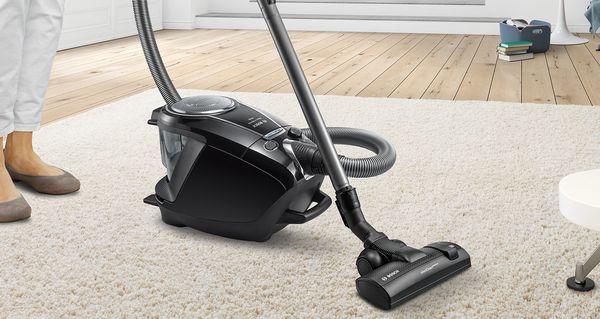 Eine Frau staubsaugt ein Wohnzimmer mit einem Bosch Bodenstaubsauger.