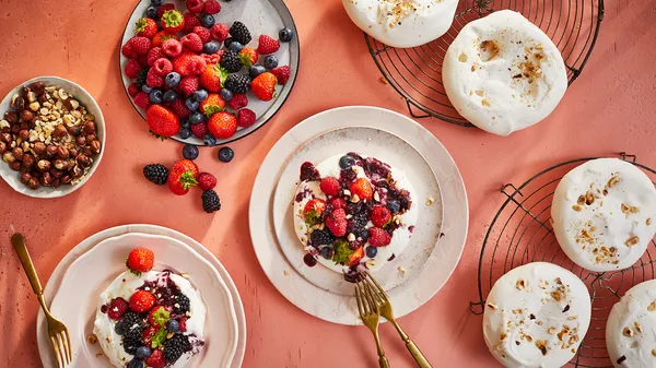 Auswahl an frischen Beeren, Granola und Backwaren auf einem leuchtend orangen Hintergrund.