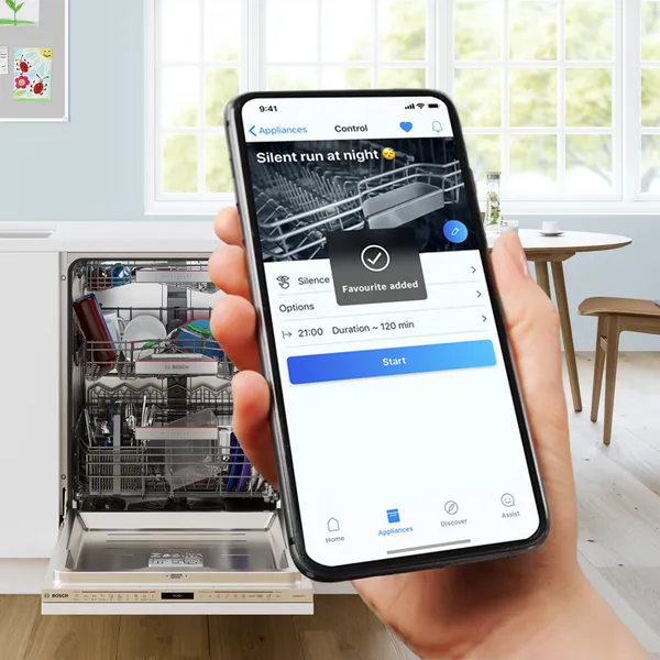 O persoană ține un smartphone pe care este afișată o aplicație pentru mașina de spălat vase, setată să funcționeze silențios noaptea, cu ușa mașinii de spălat vase deschisă.