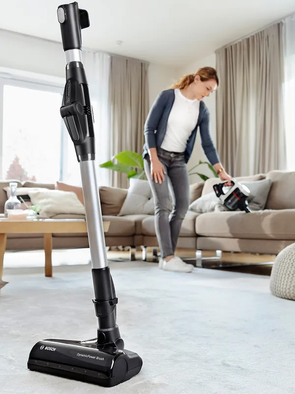 Ultimate bosh cordless vacuum cleaner in front of a woman who is vacuuming the sofa.