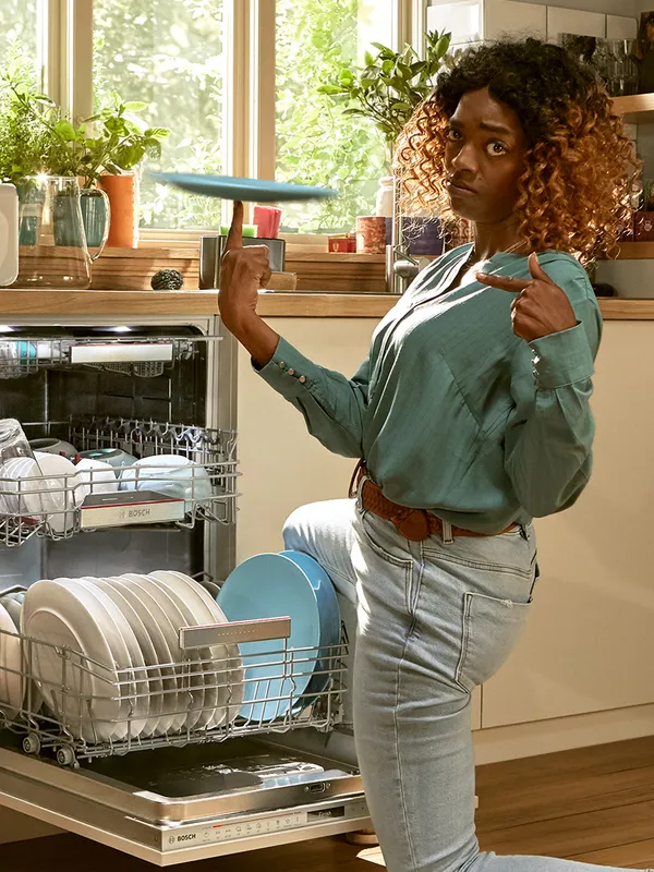 Woman in front of a loaded dishwasher twisting a plate on her finger.