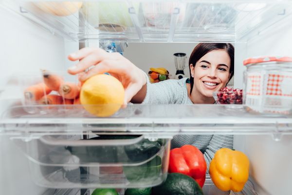 Refrigerator from inside with woman taking a fruit out of it