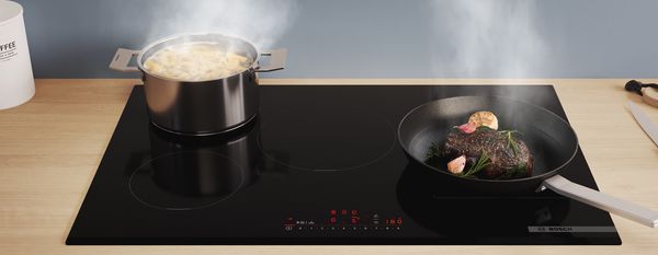 Ein Topf mit Pasta und eine Pfanne mit einem Steak auf einem Induktionskochfeld.