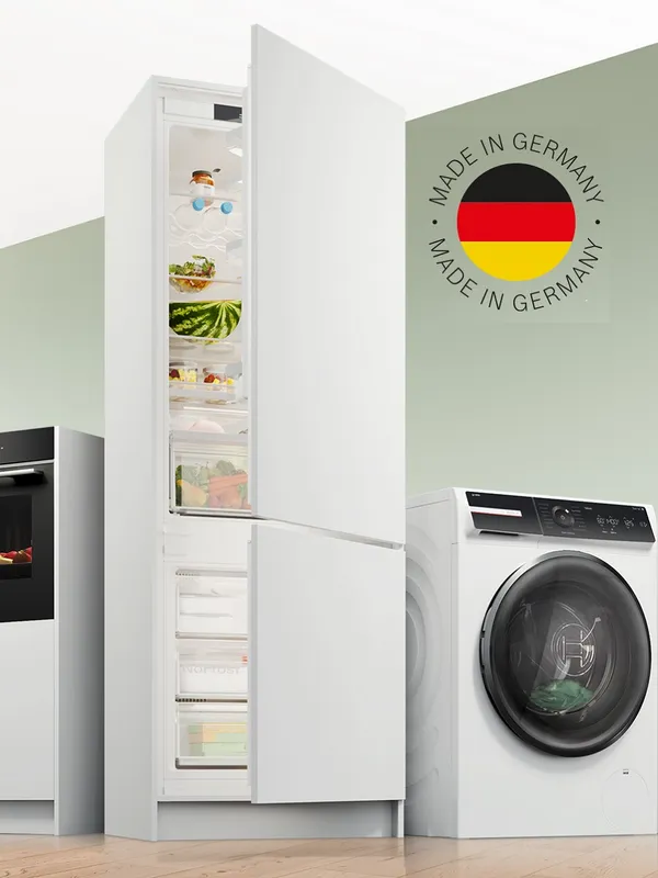 Un moderno frigorifero bianco con la porta aperta che mostra cibo fresco, accanto a una lavatrice elegante con marchio Made in Germany