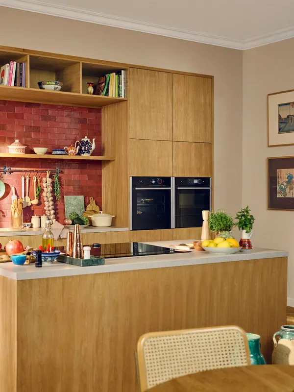 Køkken i lyst birketræ med en kogetop i køkkenøen og to indbygningsovne i de høje skabe i baggrunden