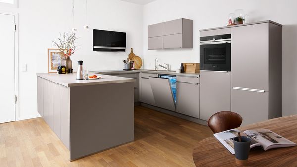 Cocina moderna con armarios grises, electrodom&eacute;sticos de acero inoxidable y suelo de madera.