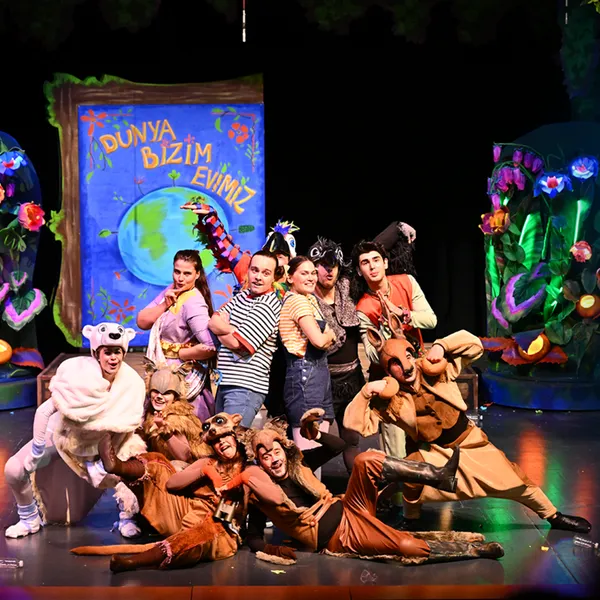 Kostümde performans grubu ile renkli sahne performansı, canlı arka damla ve props ile çevrili.