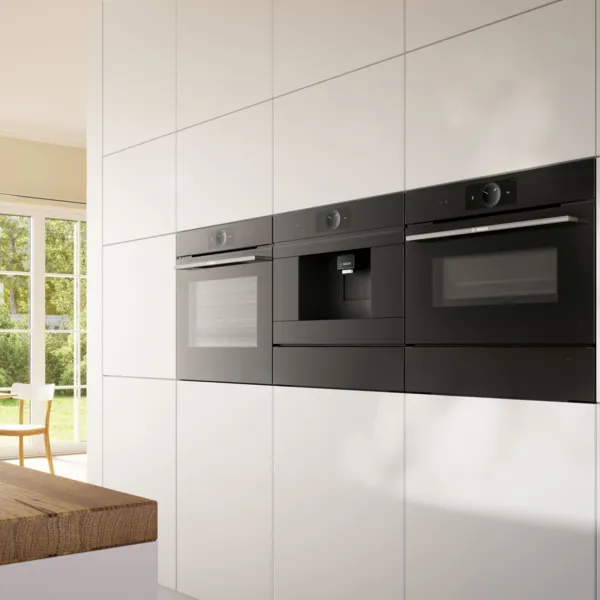 Angolo di una cucina moderna con forni neri da incasso e una finestra sul fondo