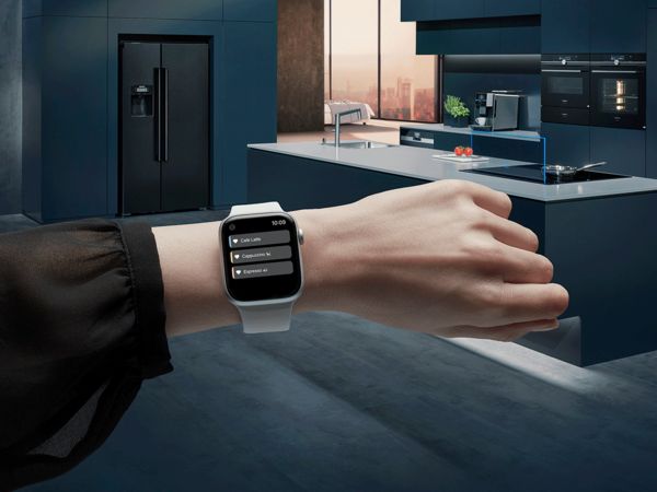 An Apple Watch on a wrist against a background of dark blue kitchen