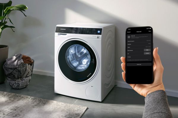 Een smartphone met de HomeWizard Energy-app, op de achtergrond een wasmachine en volle wasmand.