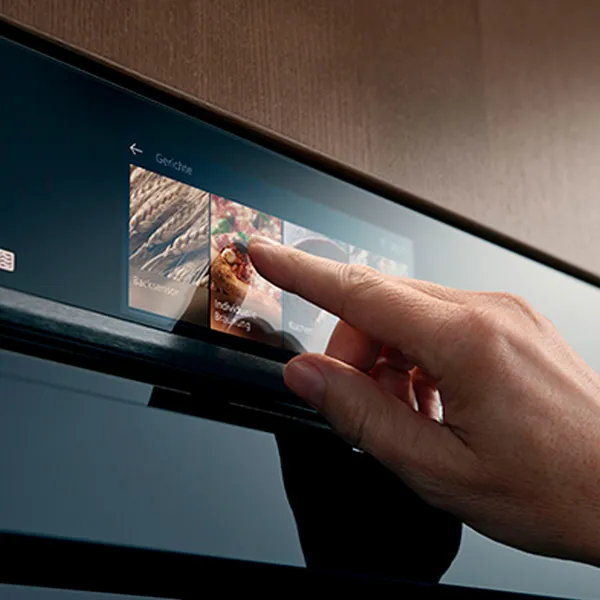 En hånd rører ved ovnens moderne touchscreen og vælger de tilberedningsmuligheder, der vises på panelet.